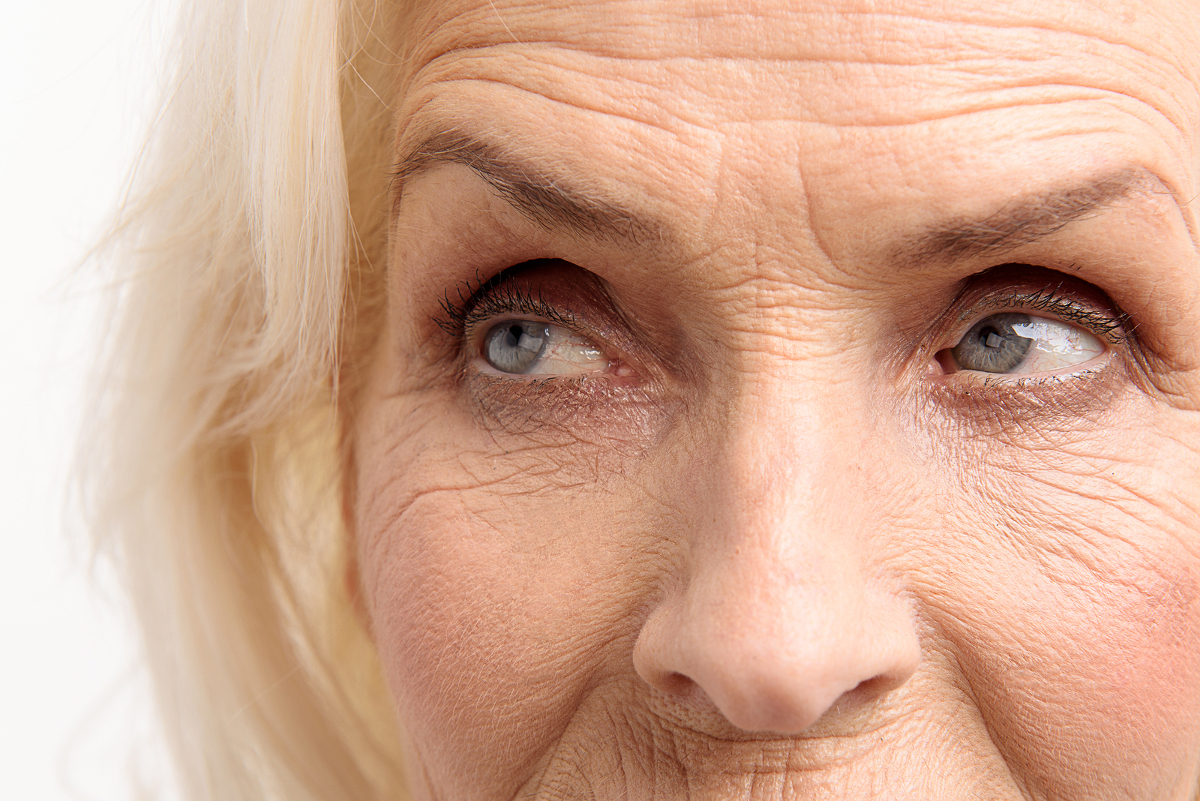 Old lady is looking aside with attention. Close up of her bright eyes